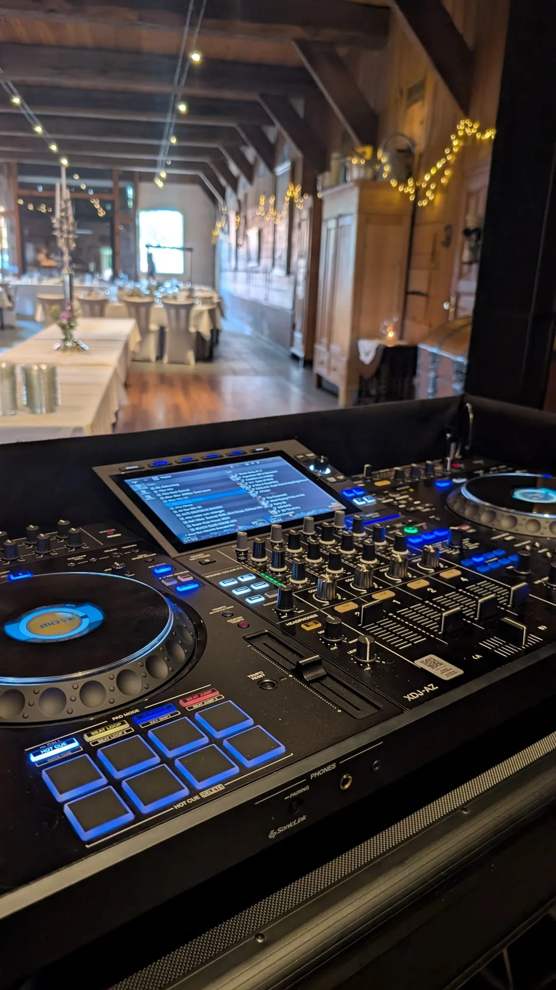 Pioneer-DJ-Controller vor einer Hochzeitslocation mit Holzgebälk und Lichterketten