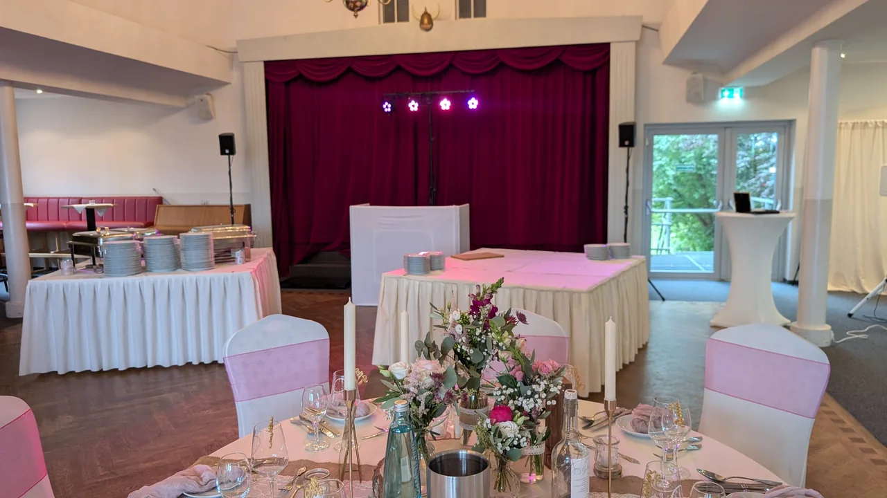 Hochzeitslocation mit festlich gedecktem Tisch und weißem DJ-Pult