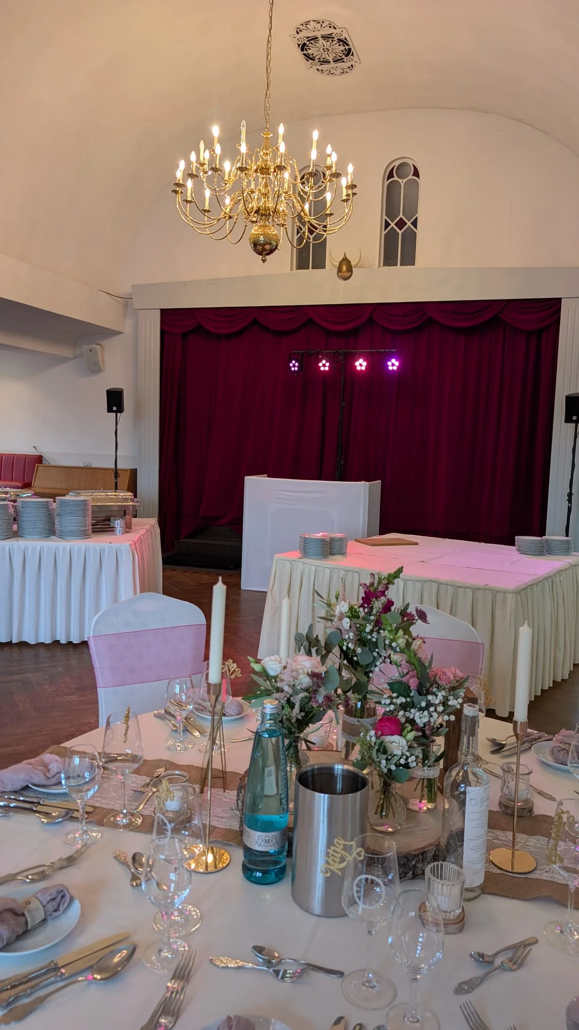 Festlich gedeckter Hochzeitstisch mit Blumenschmuck und DJ-Aufbau im Hintergrund